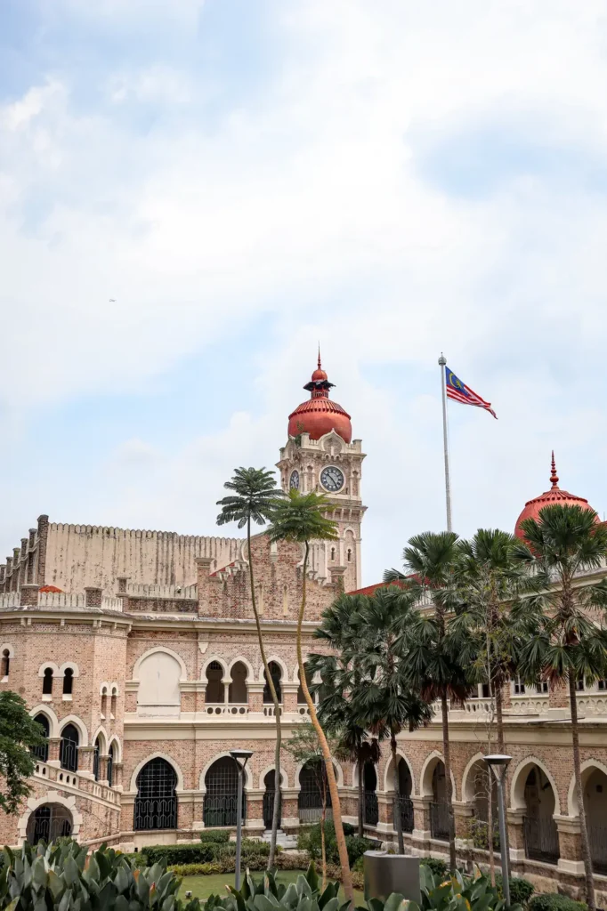 Historical Sultan Abdul Samad Building with its iconic clock tower and Malaysian flag in Kuala Lumpur under a partly cloudy sky.