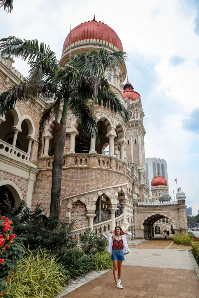 Historical Sultan Abdul Samad Building with its iconic clock tower and Malaysian flag in Kuala Lumpur under a partly cloudy sky.