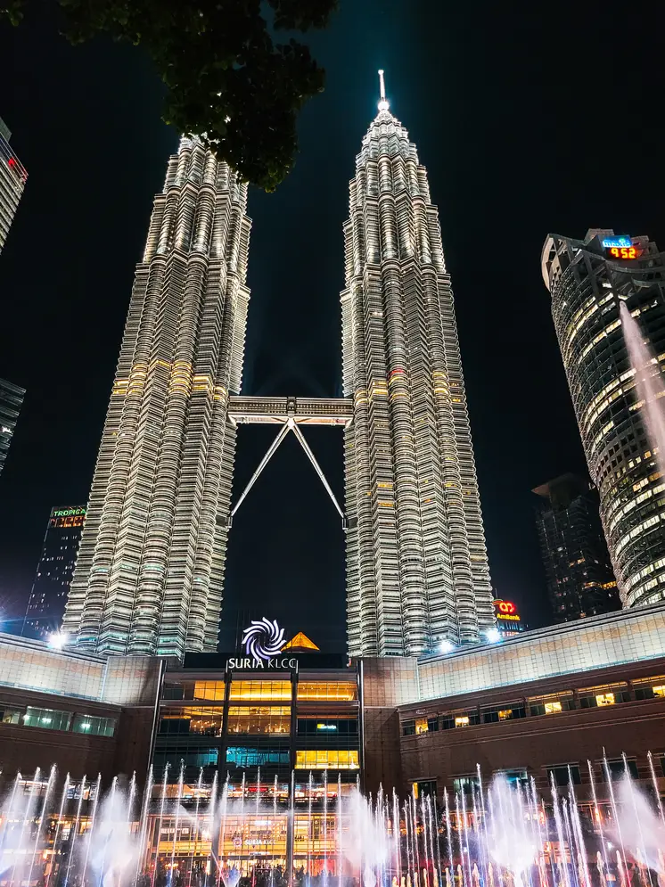 Petronas Twin Towers illuminated at night with the Suria KLCC mall and the dancing fountain display in the foreground.