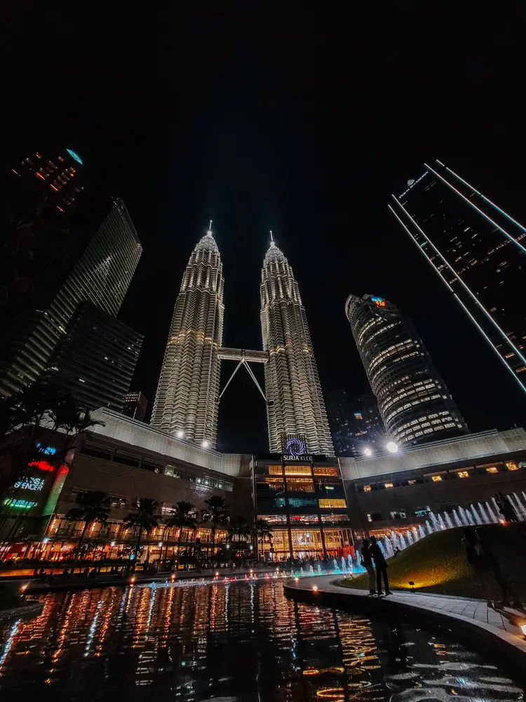 Petronas Twin Towers illuminated at night with the Suria KLCC mall and the dancing fountain display in the foreground.