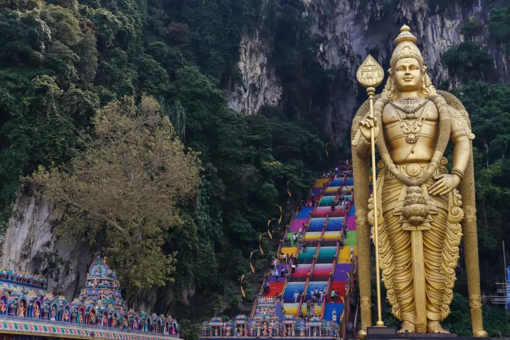 The towering golden statue of Lord Murugan standing in front of the colourful staircase leading up to Batu Caves, surrounded by lush greenery