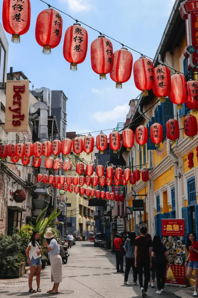 Street decorated with hanging red lanterns in the Kwai Chai Hong area of Kuala Lumpur, lined with colourful heritage buildings and people exploring