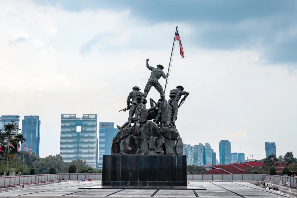 The National Monument in Kuala Lumpur, a sculpture of soldiers holding the Malaysian flag, with city skyscrapers in the background