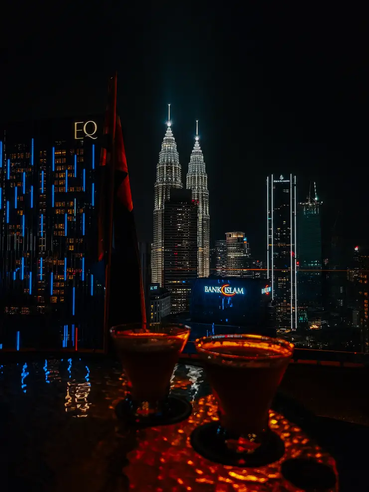 Two cocktails on a table with a night view of the Petronas Twin Towers from Helipad Rooftop Bar in Kuala Lumpur