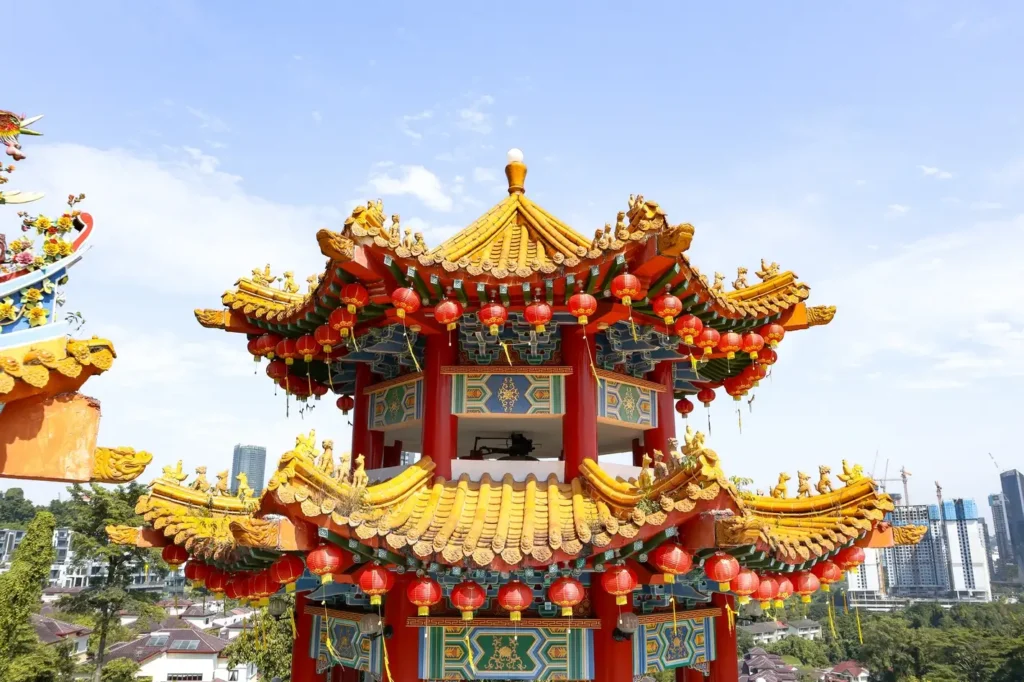 A close-up of the ornate roof of Thean Hou Temple adorned with red lanterns and intricate details, set against a bright blue sky.