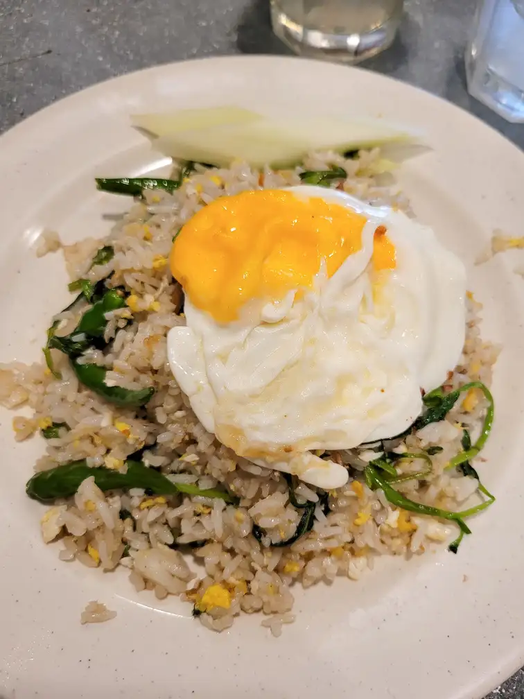 A plate of fried rice topped with a sunny-side-up egg, served with fresh greens on the side in a local restaurant in Kuala Lumpur.