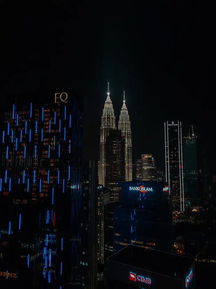 A stunning night view of Kuala Lumpur's skyline, highlighting the brightly lit Petronas Twin Towers with surrounding modern skyscrapers.