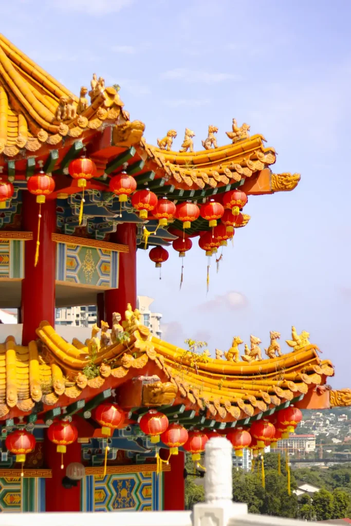 The multi-tiered structure of Thean Hou Temple in Kuala Lumpur adorned with traditional Chinese decorations and red lanterns, with city buildings in the distance.