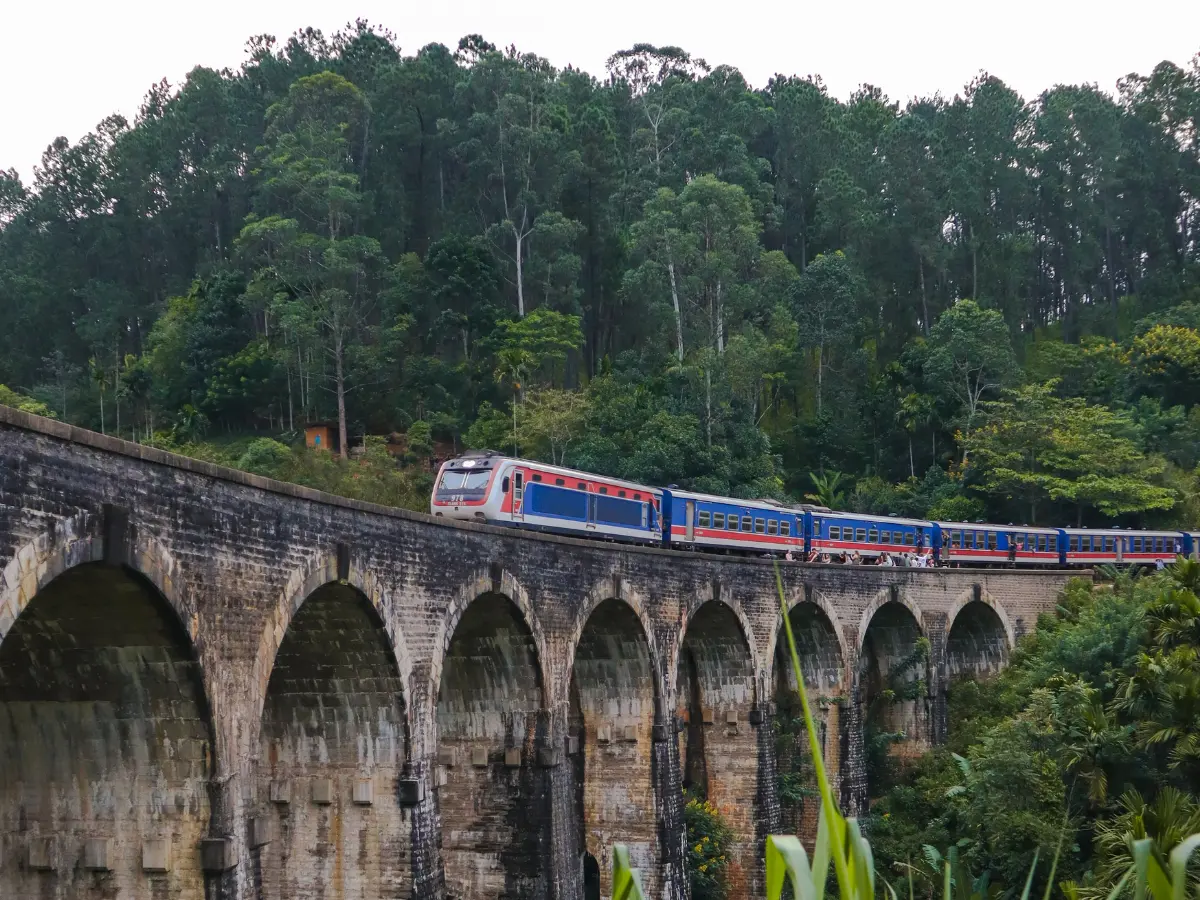 A scenic view of the iconic Nine Arches Bridge in Ella, Sri Lanka, with a train passing over its stone arches, surrounded by lush greenery and forested hills