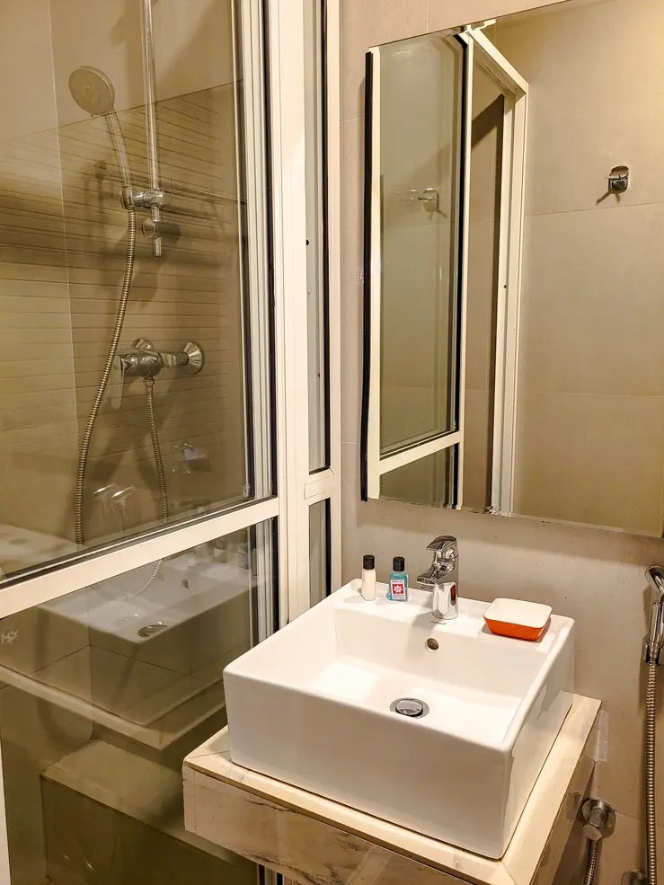 A modern bathroom featuring a white sink, a glass-enclosed shower, and small toiletries. An example of the comfortable amenities available in hotels in Kandy for travelers.