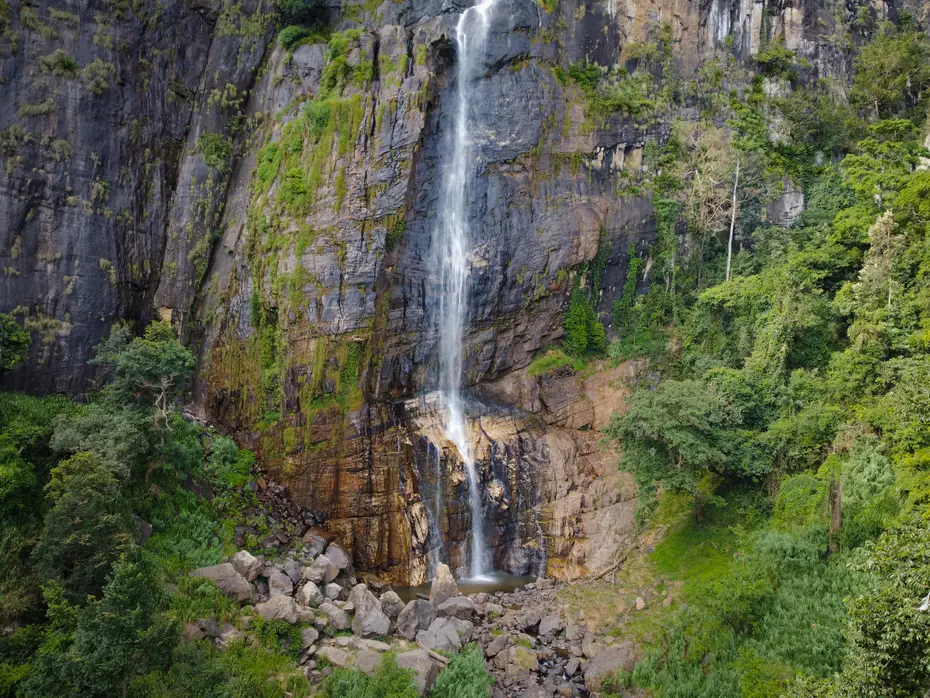 A close-up view of the base of Diyaluma Falls in Ella, Sri Lanka, where the water gracefully flows over rocks into a serene pool, framed by dense forest