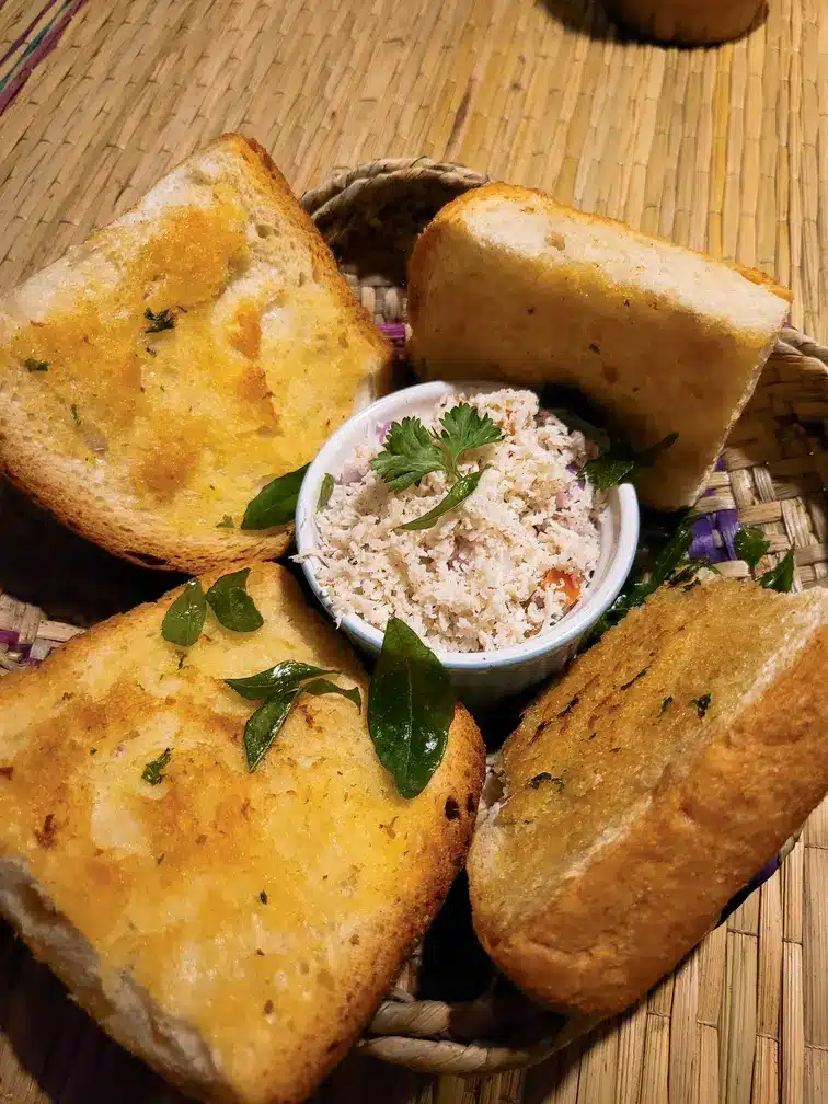 A rustic serving of golden toasted bread garnished with herbs, accompanied by a bowl of creamy coconut sambol, a popular Sri Lankan delicacy found in restaurants in Ella