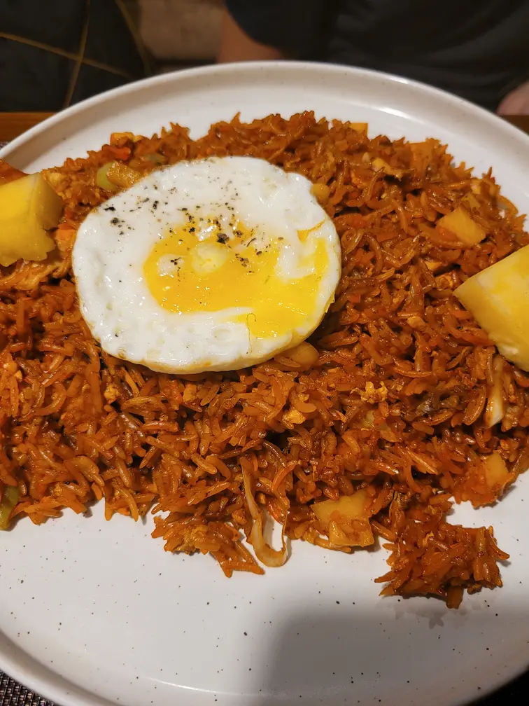 A plate of fried rice topped with a sunny-side-up egg, garnished with pineapple chunks. This image highlights the variety of flavorful dishes available in restaurants in Kandy.