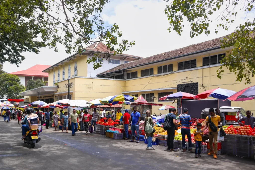 A street view of Kandy’s Central Market, bustling with shoppers and colorful vendor stalls selling fresh fruits and vegetables. This market is a vibrant hub and one of the top things to do in Kandy.