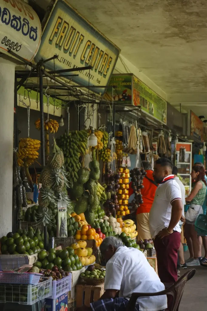 A fruit vendor at Kandy’s Central Market, surrounded by a vibrant display of bananas, pineapples, and other fresh produce. A key attraction for visitors exploring what to do in Kandy.