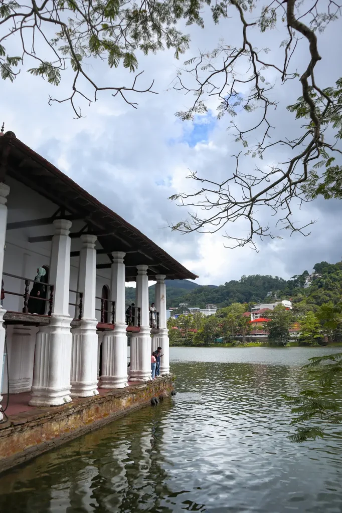 A lakeside pavilion with white columns and a tiled roof overlooking Kandy Lake, surrounded by lush greenery. Visiting this serene spot is one of the peaceful things to do in Kandy.