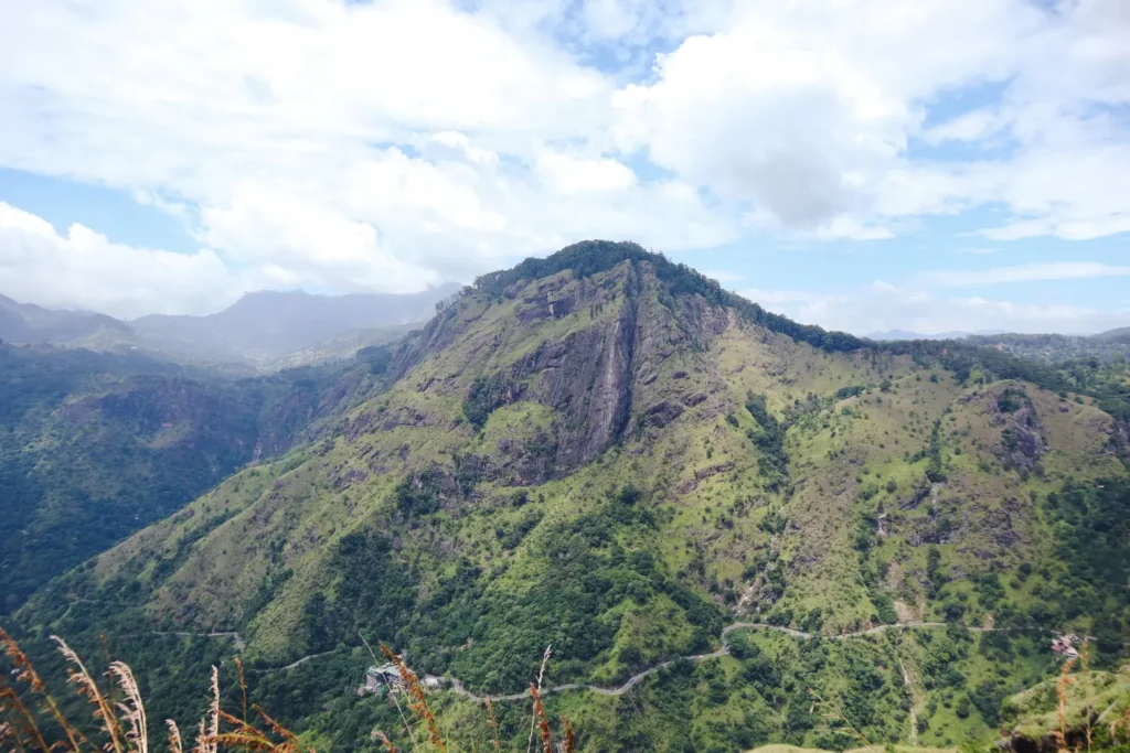 A stunning panoramic view from Little Adam's Peak in Ella, Sri Lanka, showcasing its lush greenery, rugged cliffs, and winding paths under a bright blue sky