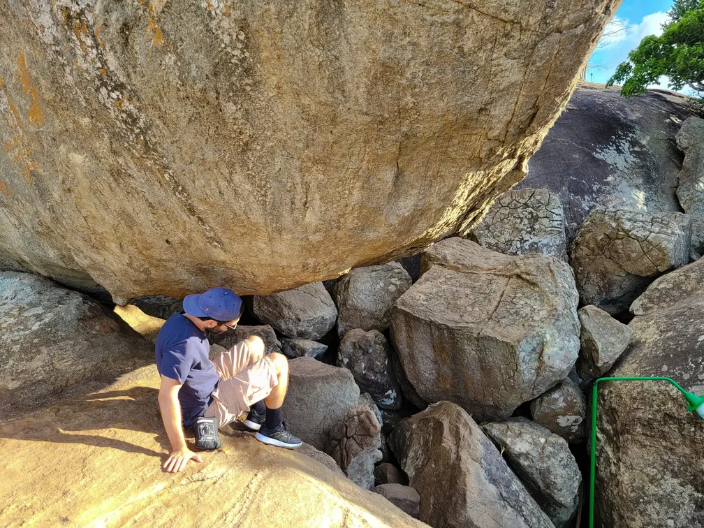 A hiker sitting under a large boulder near the summit of Pidurangala Rock, surrounded by massive rocks and uneven terrain. This resting point showcases the rugged beauty of the Pidurangala Rock hike.