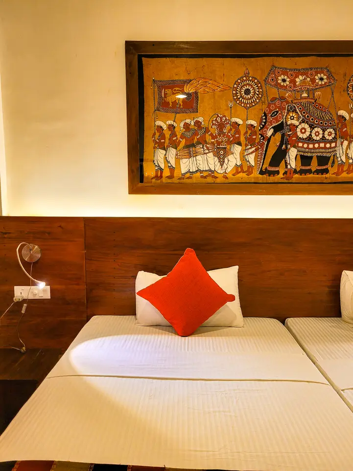 A cozy hotel room featuring a wooden headboard, bright red accent pillow, and a large decorative painting