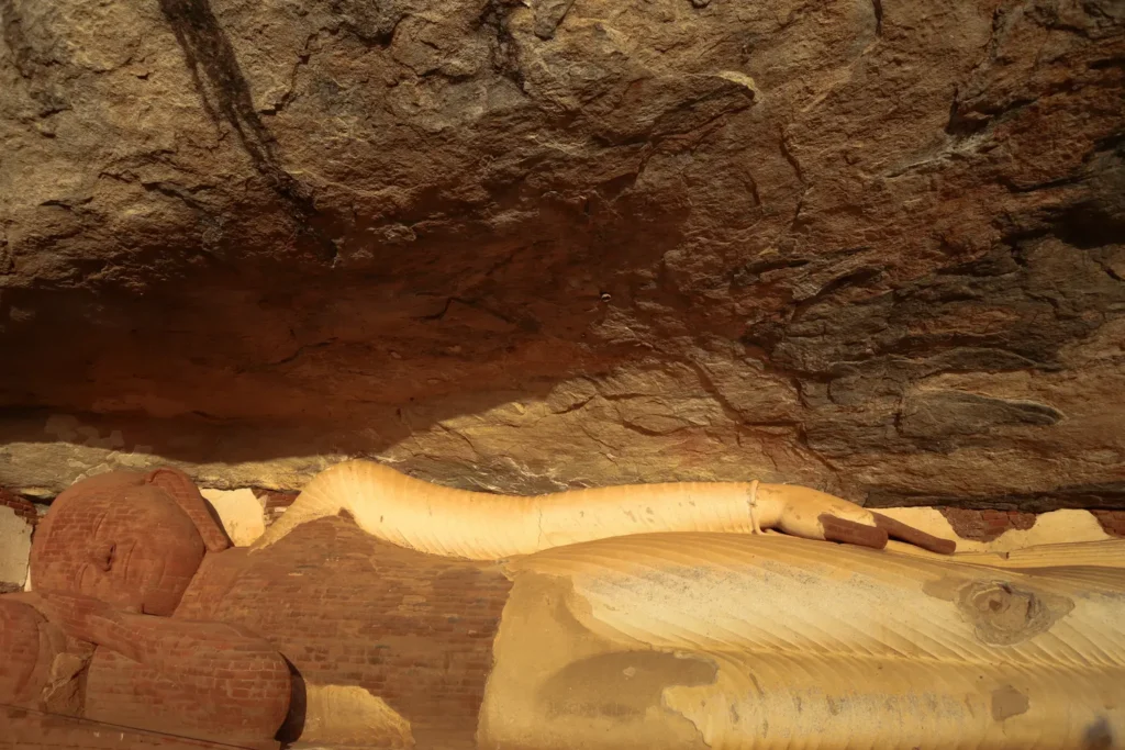 The serene and weathered Reclining Buddha statue nestled beneath a massive rock overhang at Pidurangala Rock.