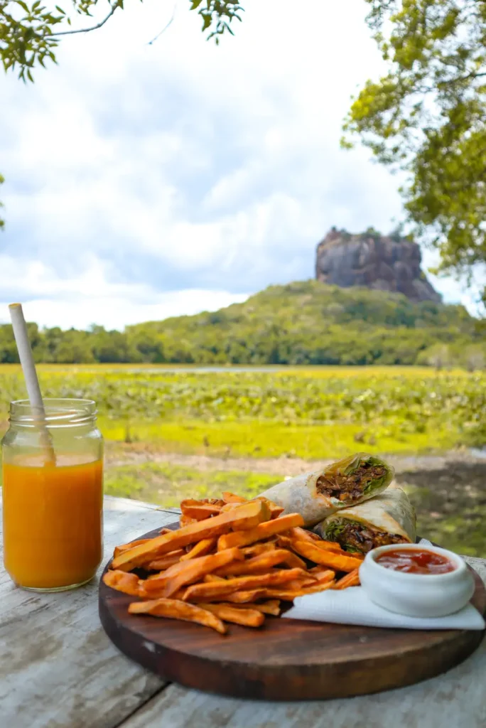 A wooden table set with a fresh meal featuring a wrap filled with vegetables and protein, served alongside crispy sweet potato fries with ketchup and a refreshing glass of orange juice. 