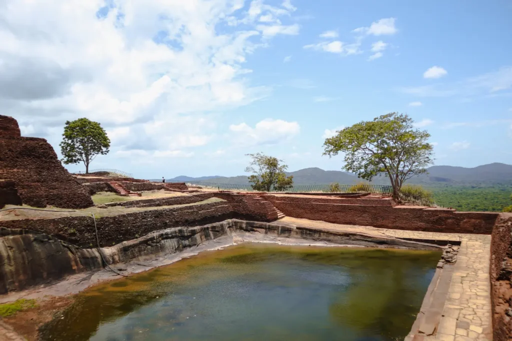 "The remains of an ancient pool atop Sigiriya, the Lion Rock fortress in Sri Lanka, surrounded by red-brick walls and terraced gardens.