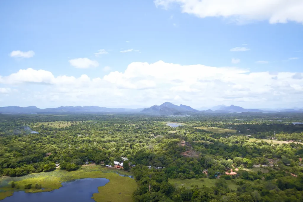 A breathtaking aerial view of the lush green landscapes, lakes, and distant mountains surrounding Sigiriya, Sri Lanka, as seen from the top of Lion Rock