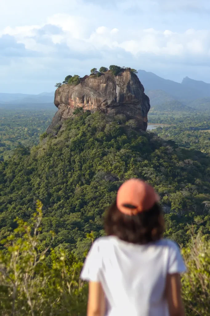 A person in a white shirt and pink cap gazing at the iconic Lion Rock in Sigiriya from the vantage point of Pidurangala Rock