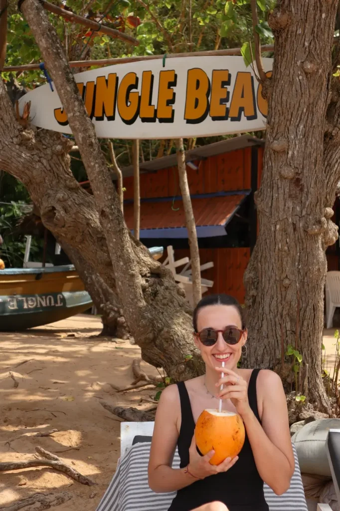 Mariana enjoying a fresh coconut under a “Jungle Beach” sign, highlighting one of the hidden and chill places to visit in Mirissa.