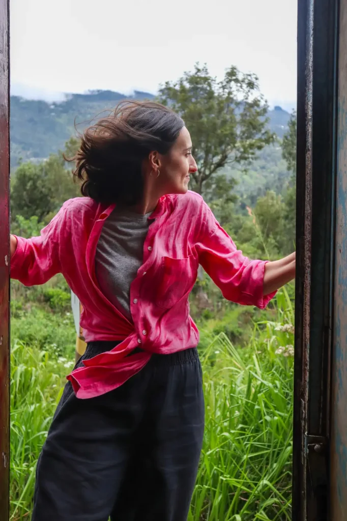 Mariana enjoying the open doorway of a moving train on the kandy to ella route, with mountain views and wild greenery in the background. This legendary train ride offers a unique way to experience Sri Lanka’s highlands.