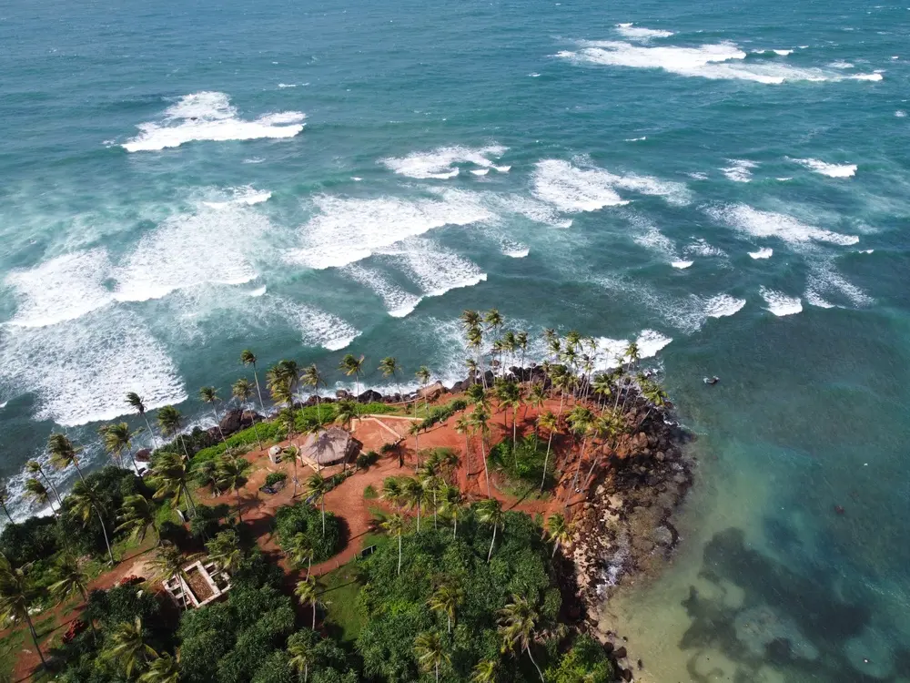 A drone view of the iconic red cliff dotted with palm trees at Coconut Tree Hill, one of the most photographed and unmissable places to visit in Mirissa.