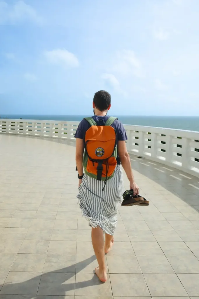 A traveler walks barefoot along a tiled walkway overlooking the sea, wearing a sarong and carrying sandals—capturing the laid-back vibe and cultural experiences that make up the best things to do in Mirissa.