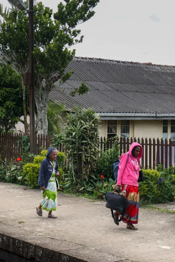 Two women in colorful skirts and hoodies walk along a train platform lined with plants and flowers. It’s a quiet stop along the scenic kandy to ella train, where local life and nature intersect.