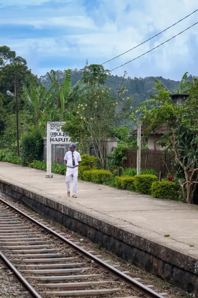 A railway staff member walks along the platform at Haputale station, surrounded by tropical greenery. This small scenic stop is part of the magical journey on the ella to kandy train.