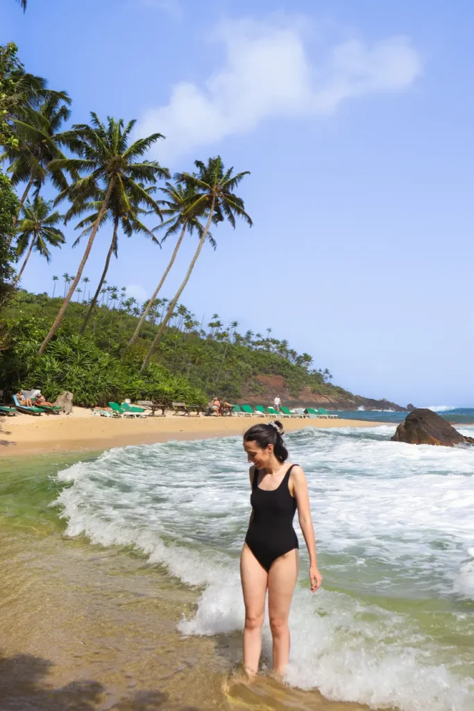 Mariana in a black swimsuit standing in the surf at Secret Beach in Mirissa, surrounded by lush greenery and beachgoers—perfect for relaxing moments and top things to do in Mirissa.