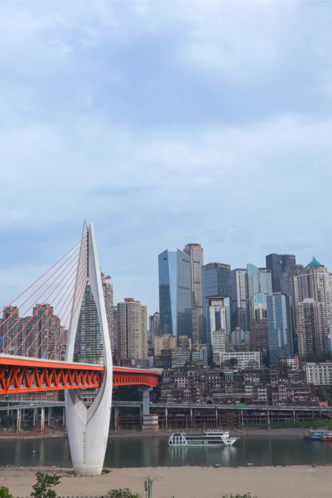 China Travel Tips: 35+ must-know things before visiting (2026 Guide) 9 Tall vertical view of Qiansimen Bridge against a backdrop of high-rises and a glassy river below, with a cruise boat in motion.
