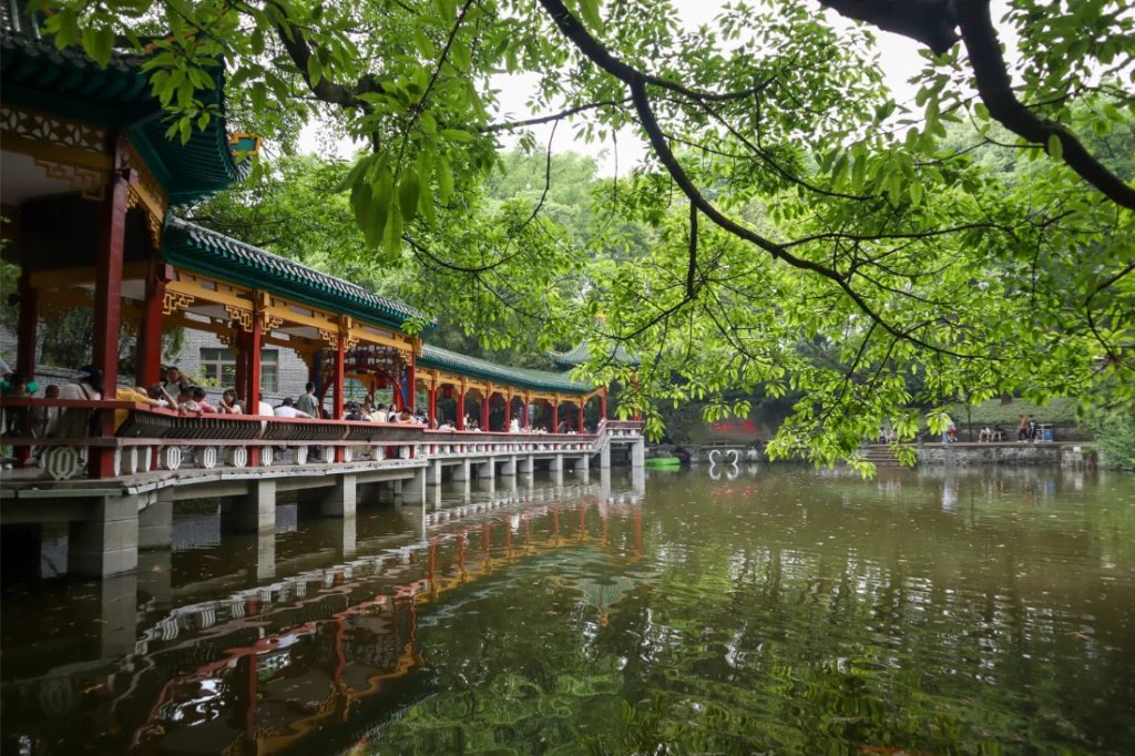 2 weeks in China: the perfect first-timer itinerary for an unforgettable trip 33 Long covered walkway with red and green traditional architecture stretches along a tranquil pond in Chongqing’s Eling Park, framed by overhanging tree branches.