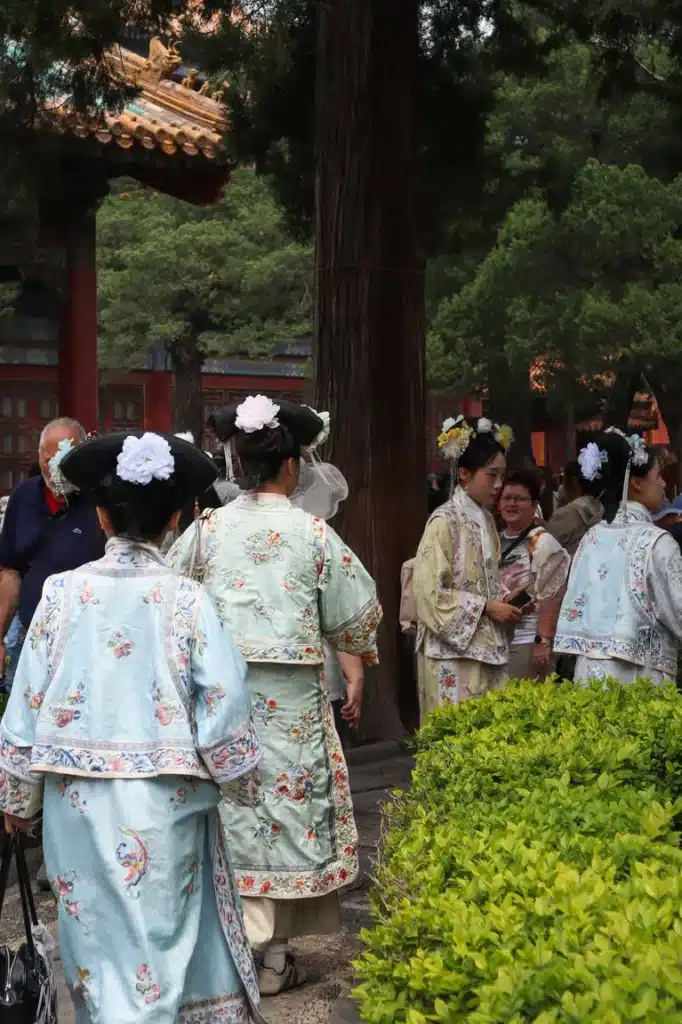 My honest review of Airalo in China 10 A group of women dressed in Qing dynasty-style clothing with embroidered pastel robes and floral headpieces walk through a garden courtyard, attracting the attention of tourists.