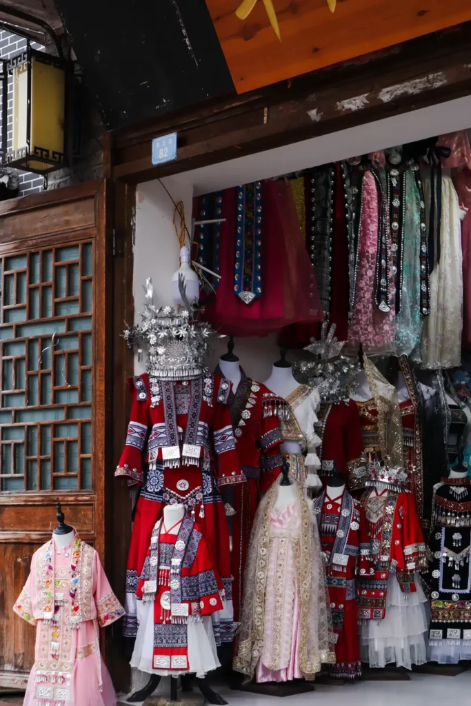 China Travel Tips: 35+ must-know things before visiting (2026 Guide) 7 A storefront in China showcases an array of ornate traditional ethnic costumes, including bright red embroidered dresses and silver headdresses. A great China travel tip is to visit local shops to admire or rent traditional attire for immersive cultural experiences.