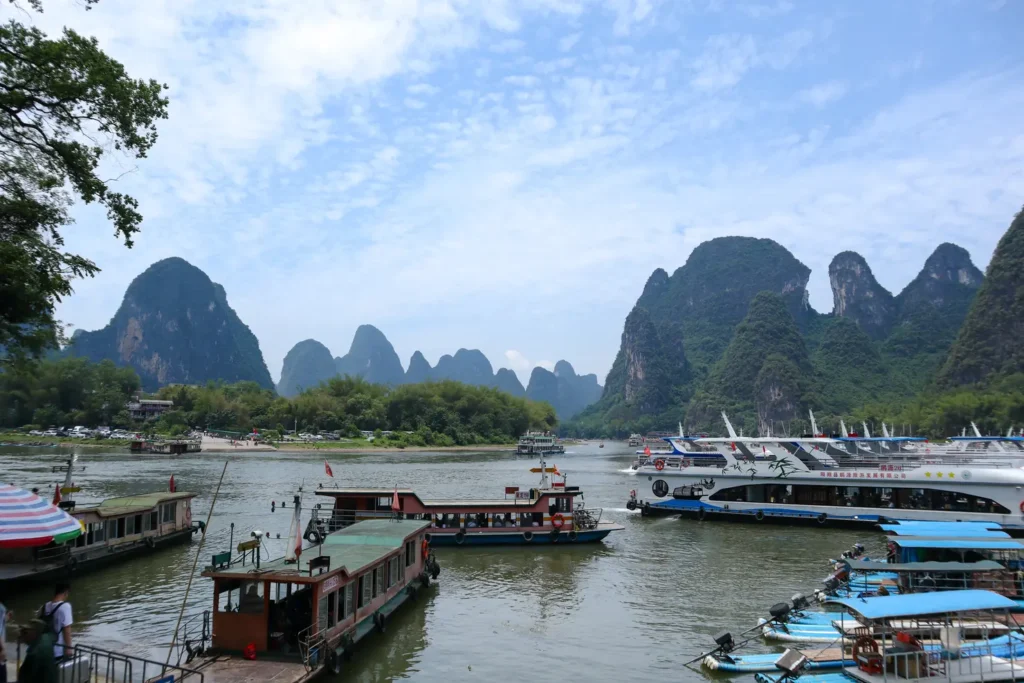 2 weeks in China: the perfect first-timer itinerary for an unforgettable trip 29 Docked tour boats and bamboo rafts line the Li River in front of a lush, mountainous skyline under a blue sky. Many travelers include a Li River cruise on a China 2 week itinerary.