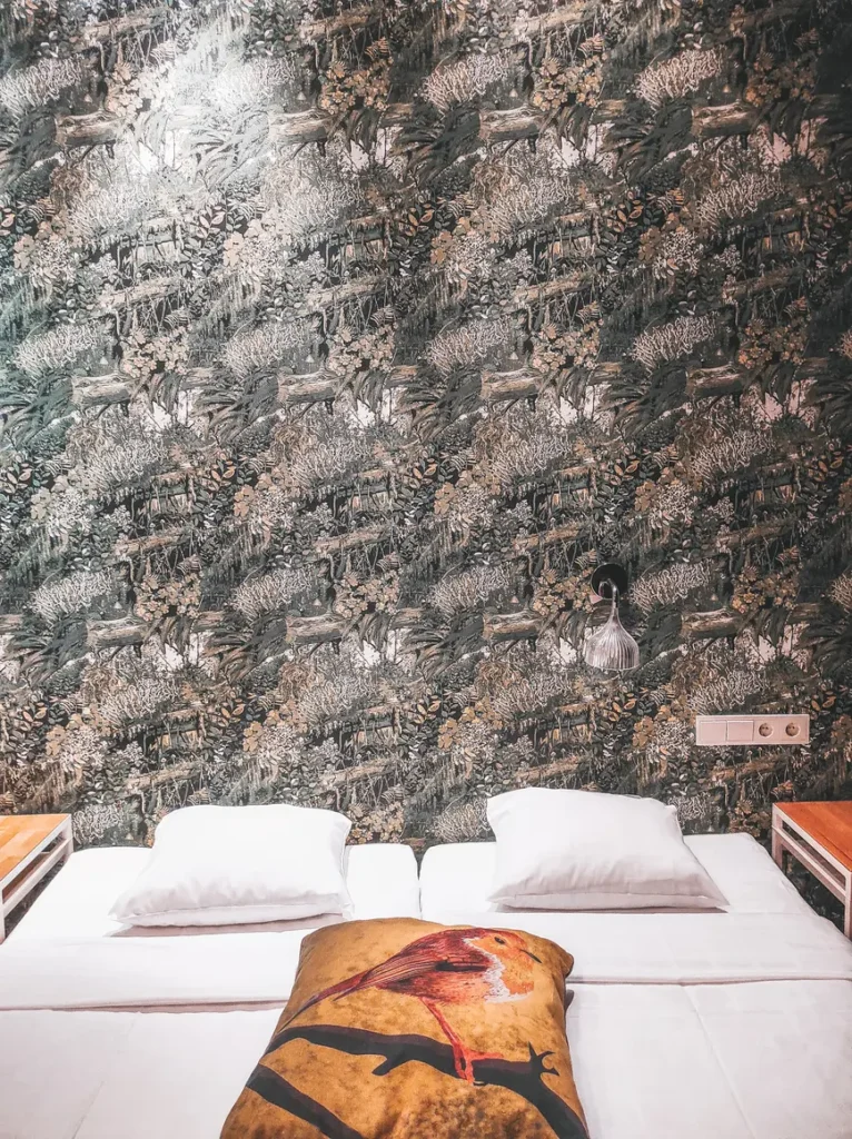 Onde ficar em Helsínquia: os melhores bairros e hotéis para a vossa estadia 11 Cozy double bed with white linens and a bird-printed throw blanket in a stylish Helsinki hotel room with forest-themed wallpaper.