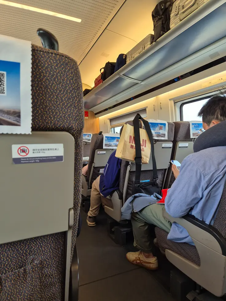 How to buy train tickets in China (2026): easy & tourist-friendly options 5 Passengers sit and relax inside a modern Chinese high-speed train cabin, with overhead luggage racks filled with bags.