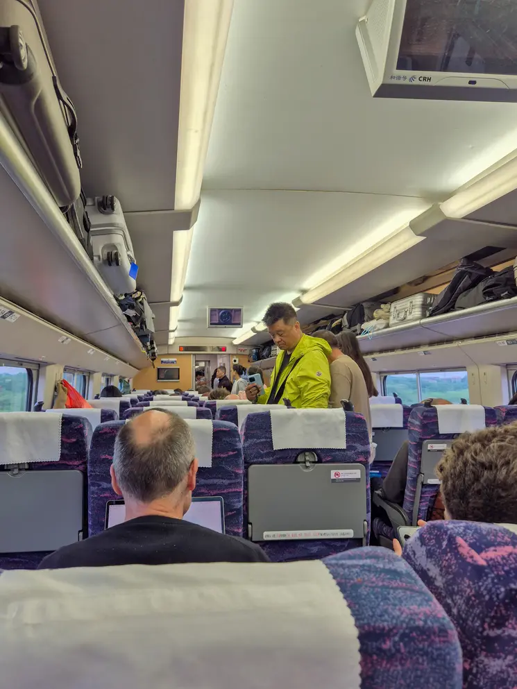 How to buy train tickets in China (2026): easy & tourist-friendly options 4 Inside a high-speed train carriage in China, travelers sit or stand in the aisle while using phones or laptops. The onboard setting offers a glimpse of what to expect for those learning how to book train tickets in China.