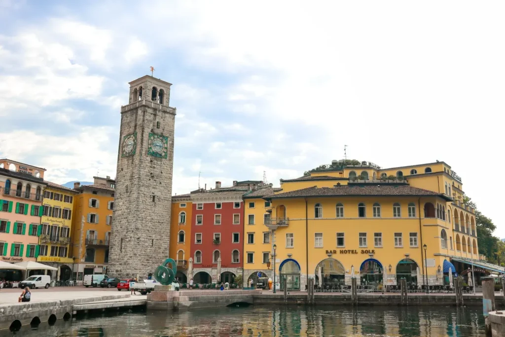 21 locais a visitar no norte de Itália que vos vão conquistar facilmente 18 The charming lakeside promenade in Riva del Garda with a stone clock tower and vibrant yellow buildings, a peaceful retreat and one of the scenic places to visit in Northern Italy.