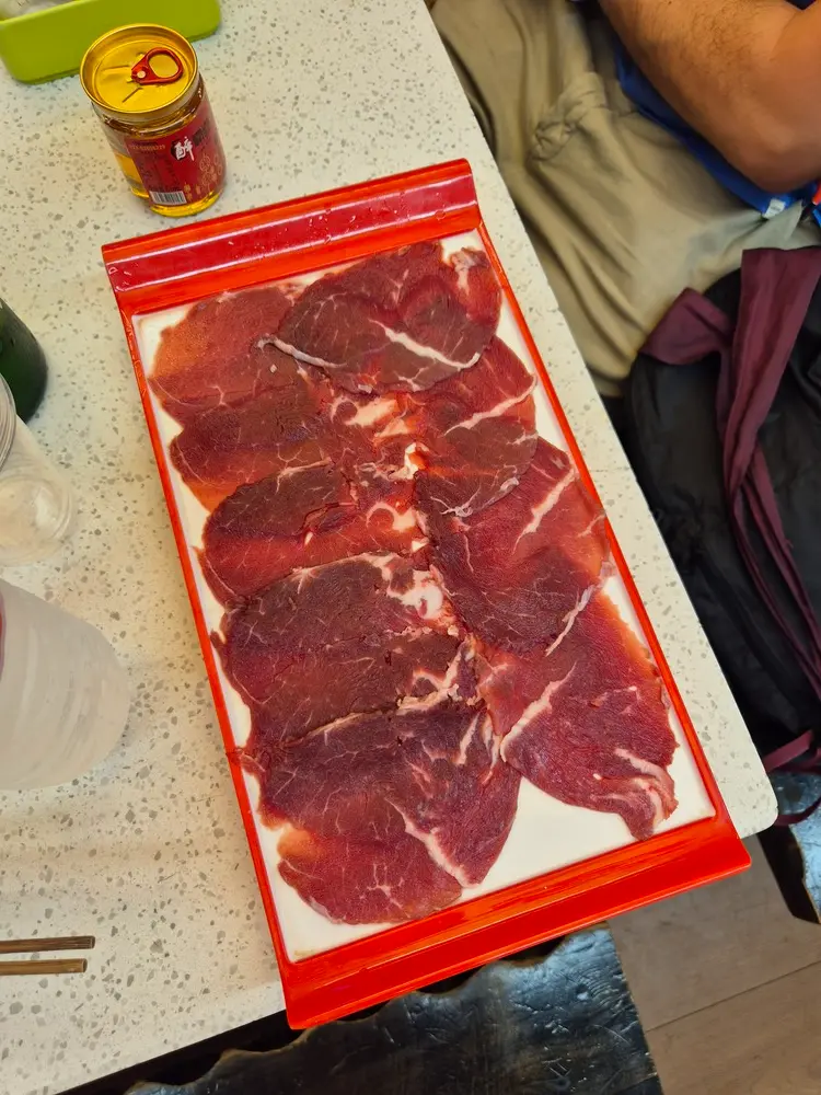China Travel Tips: 35+ must-know things before visiting (2026 Guide) 20 A tray of raw marbled beef slices is ready to be cooked, sitting on a restaurant table with condiments nearby.