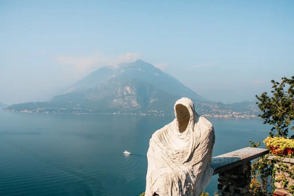 21 beautiful places to visit in Northern Italy that will steal your heart 16 Ghostly white statue overlooking Lake Como with a misty mountain in the distance, adding artistic mystery to one of the most iconic places to visit in Northern Italy.